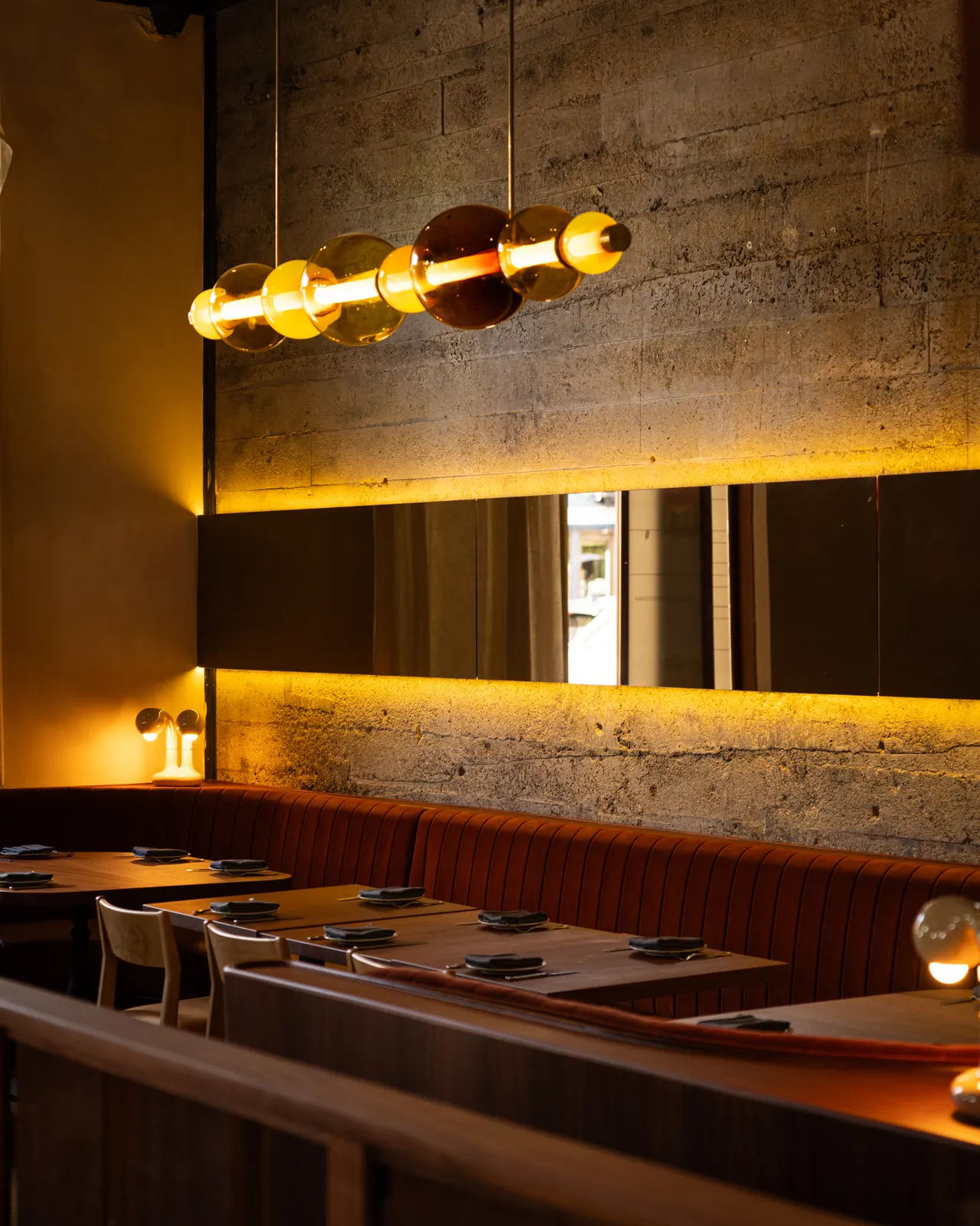 Amber glass pendants over the rust banquette and mirrored concrete wall at Amado, Burlingame
