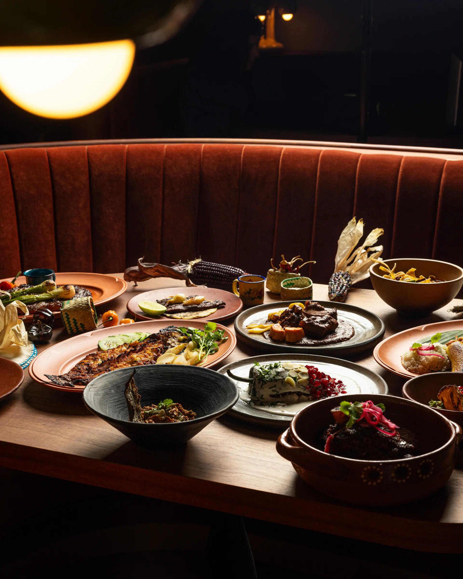 The full table set against the leather booth at Amado, Burlingame: mole, mariscos, and mezcal light