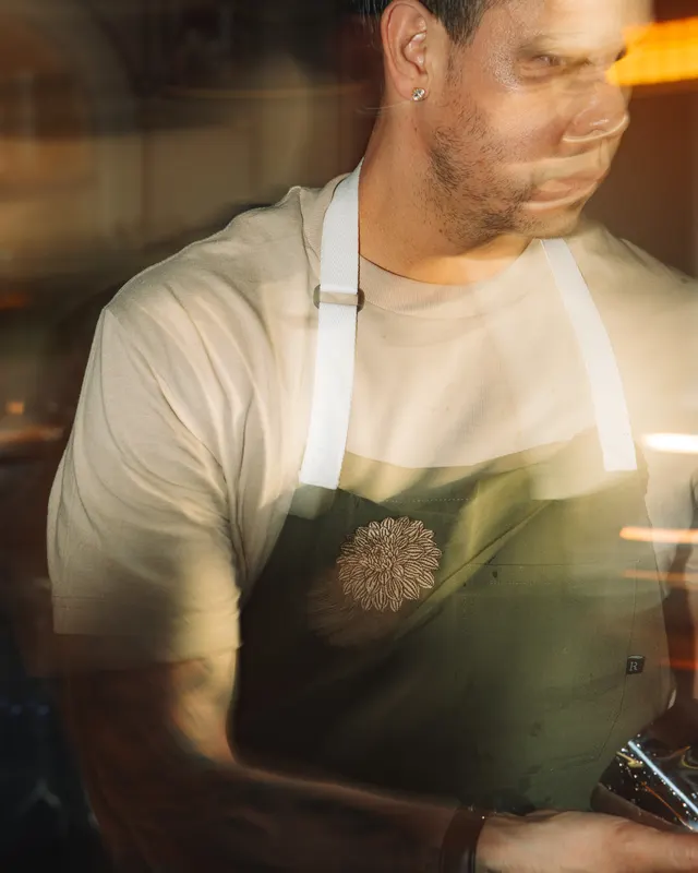 A chef in a white tee and dark apron at the pass at Amado, Burlingame, lit warm from the side