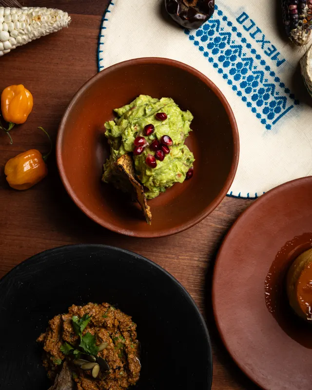 Guacamole with pomegranate in a clay bowl beside a painted plate at Amado, Burlingame