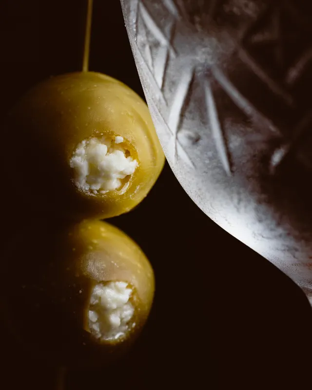 Two blue-cheese-stuffed olives on a pick beside a frosted cut-glass coupe at Amado, Burlingame