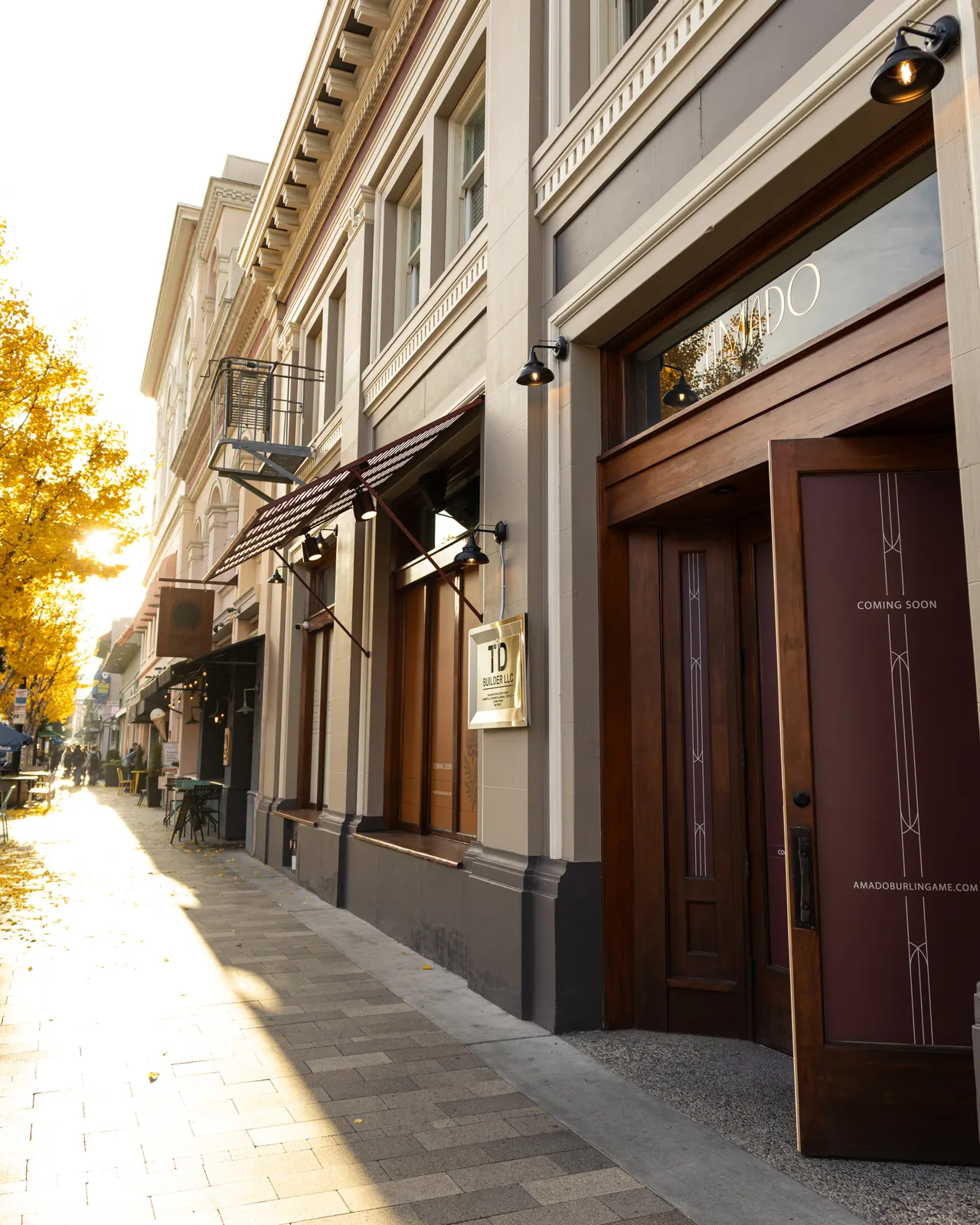 The wood-and-glass doors of Amado down a sunlit Burlingame sidewalk, the street trees gone gold