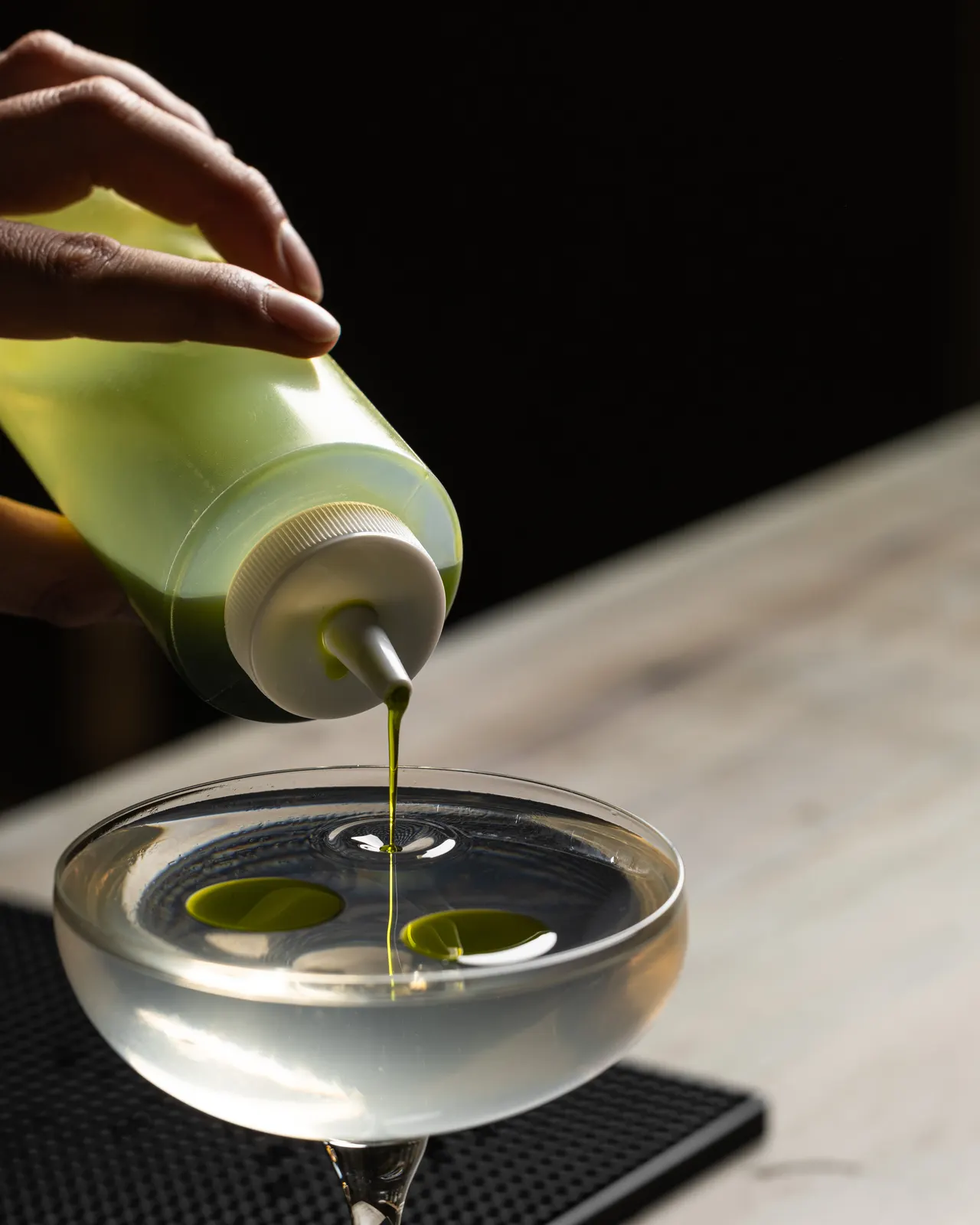 A green cordial poured from a squeeze bottle into a glass on the marble, shot for Barworks, Campbell
