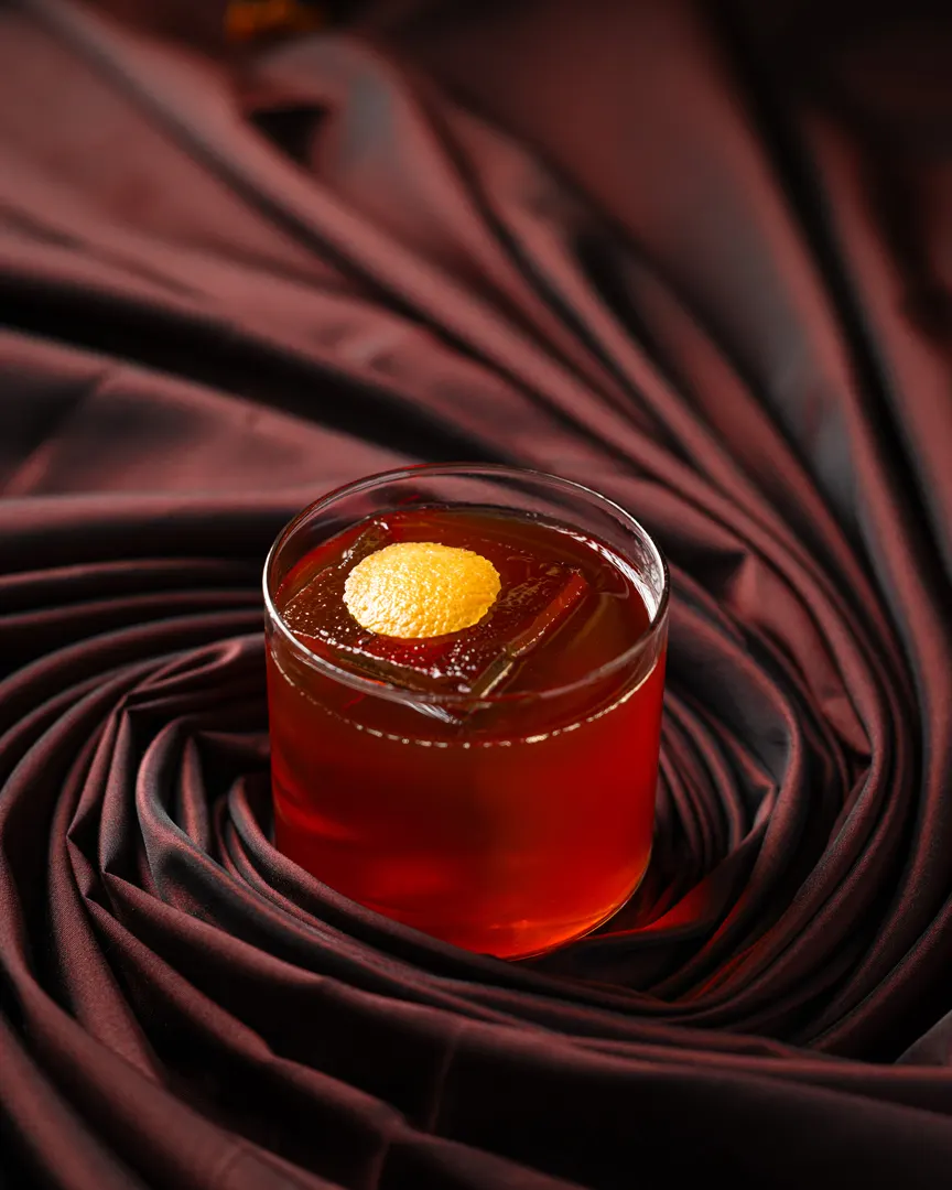 A ruby old fashioned with a dried-orange chip on crimson silk, shot for Barworks, Campbell