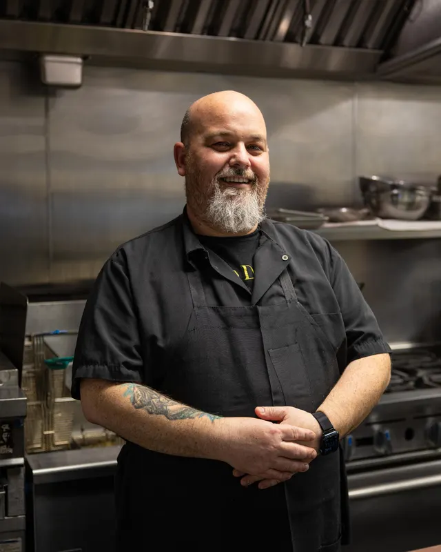 The chef, arms crossed in his kitchen, letting the beard do the talking