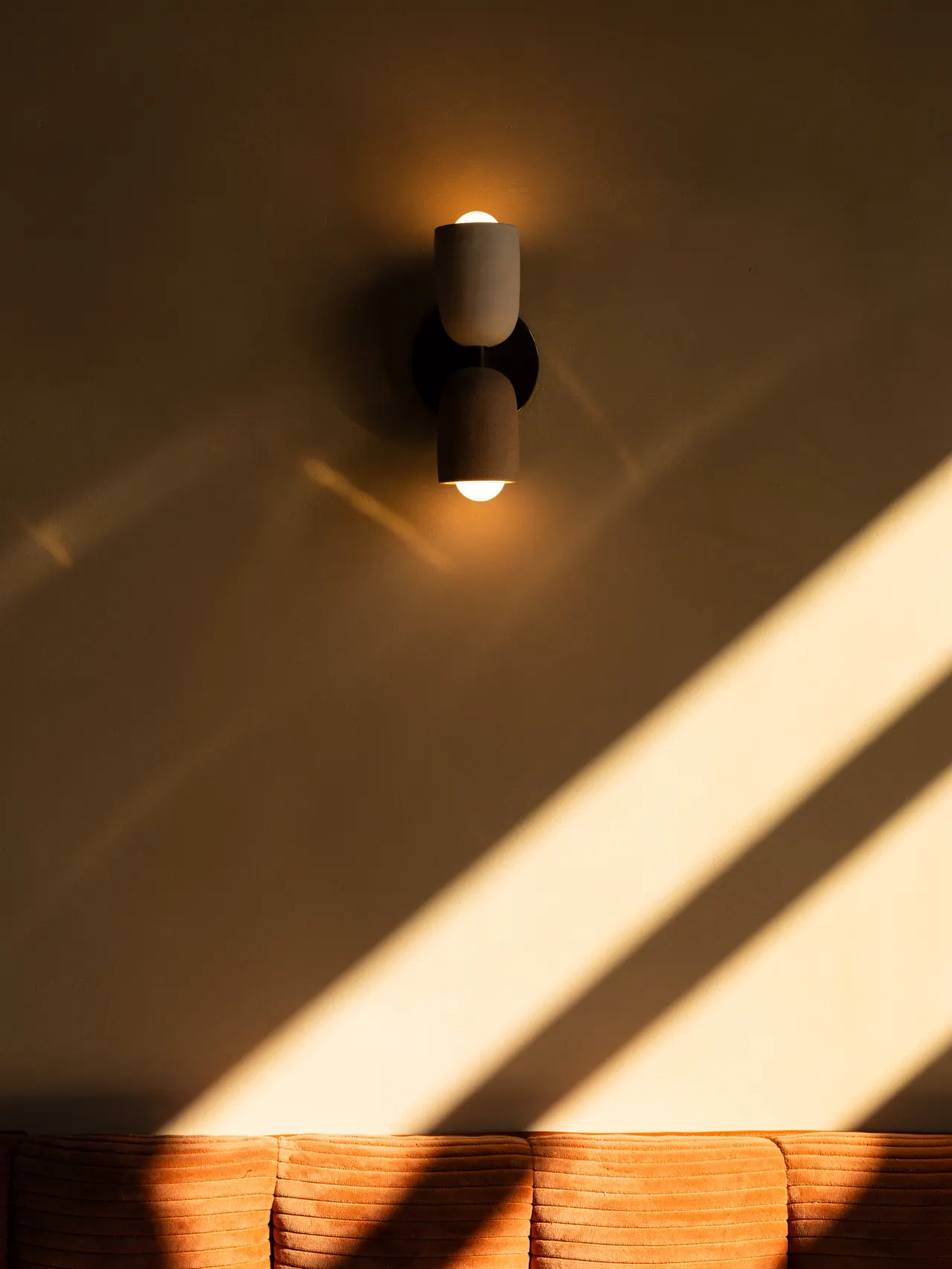 A single wall sconce over the rust banquette, late sun raking across the plaster at Casa Sofia, San Francisco