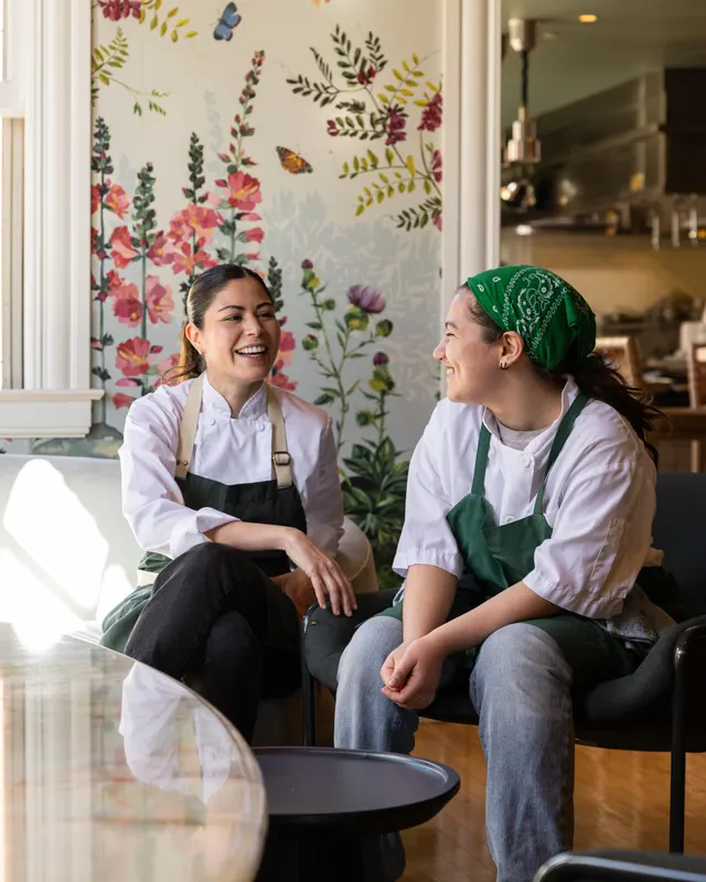 Two line cooks cracking up against the floral wallpaper