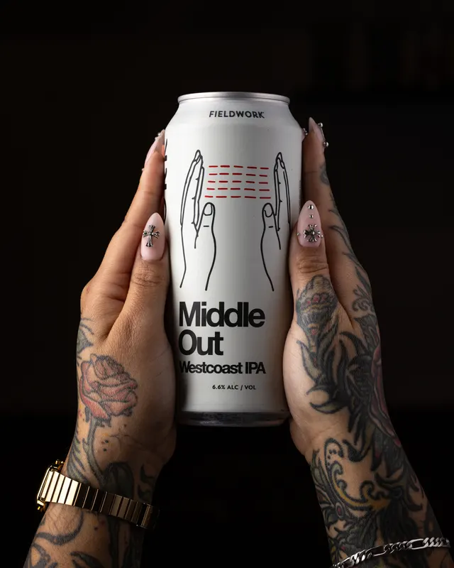 Tattooed hands presenting the Middle Out IPA for Fieldwork Brewing, San Leandro