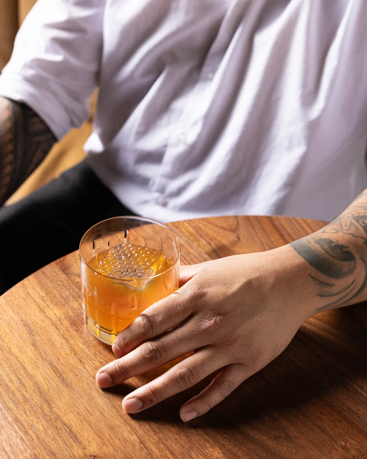 An old fashioned held in tattooed hands on the wooden bar at Honeycomb Cocktail Lounge, Livermore