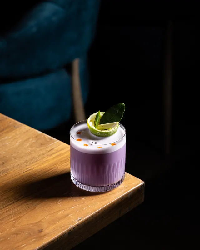 A violet sour with a lime wheel and kaffir leaf on the bar rail at Honeycomb Cocktail Lounge, Livermore