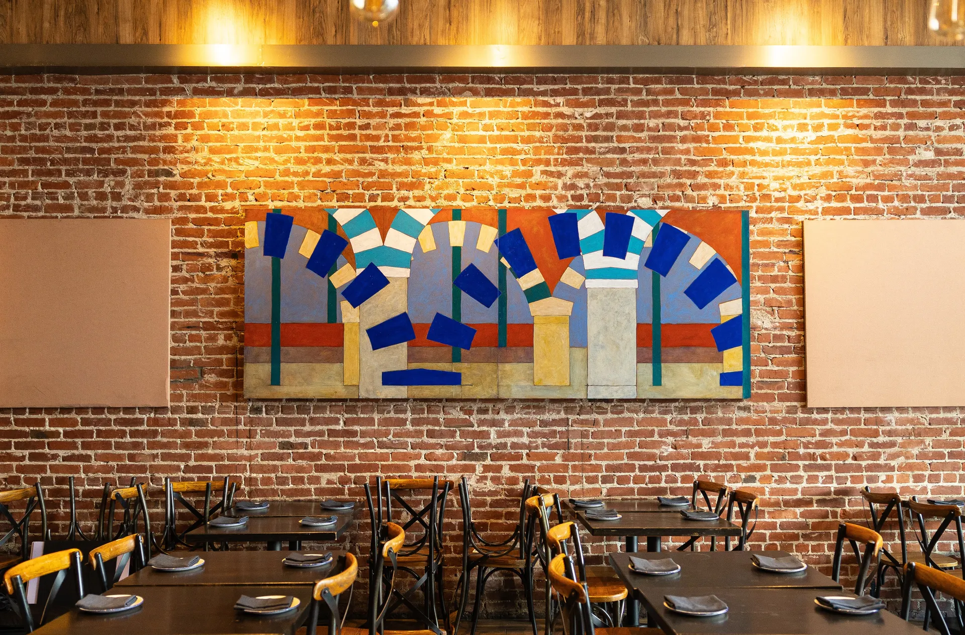The brick dining room at La Marcha, Berkeley: the arches mural over the set tables, plates down, the brass mirror catching the light