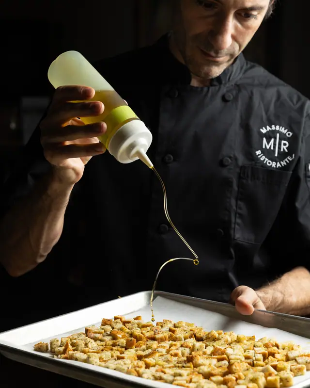 The chef drizzling olive oil over a tray of herbed croutons at Massimo Ristorante, Walnut Creek