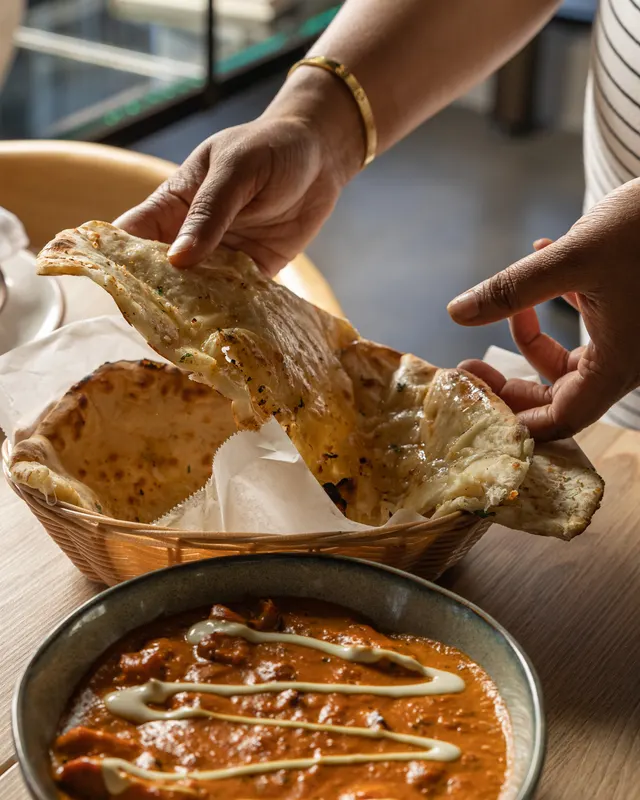 Hands tearing fresh naan over the basket at Noor Fusion Kitchen, Berkeley