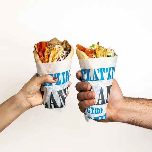 Two wrapped gyros raised like a toast against white, for Nick the Greek