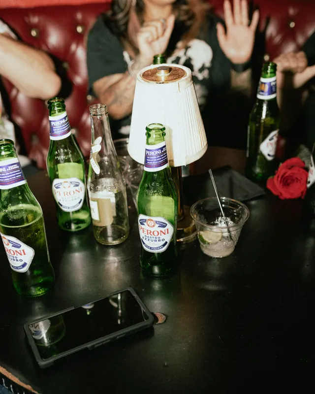Peroni bottles, a shaded lamp and a red rose on the table between hands, at the Oaxaca Open bartender competition, Oakland