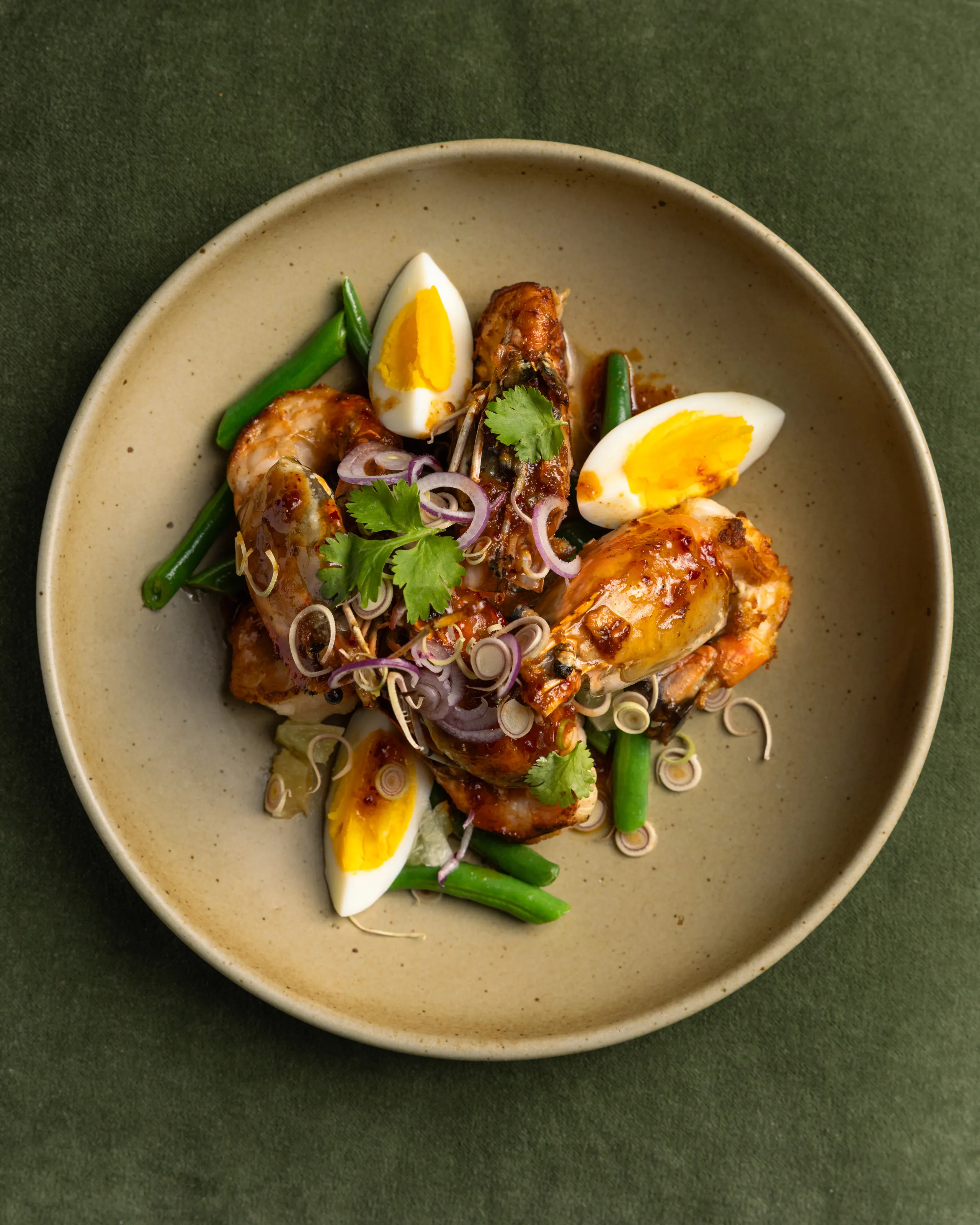 Glazed prawns with soft-boiled egg, green beans, shallot and lemongrass on a speckled plate over green linen at Payakk, Oakland