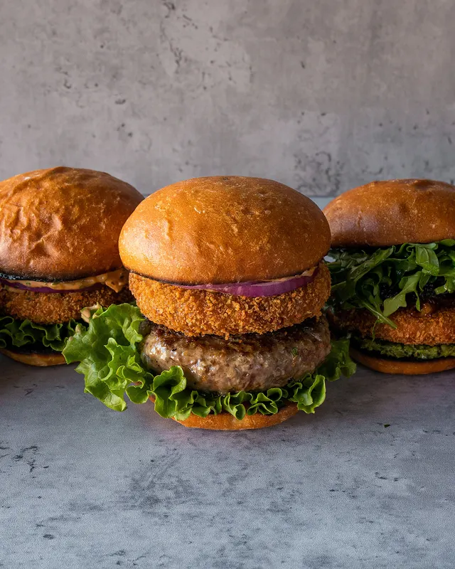 Three burger builds in a row on studio grey, one consistent look - recipe photography by Lemonad Media