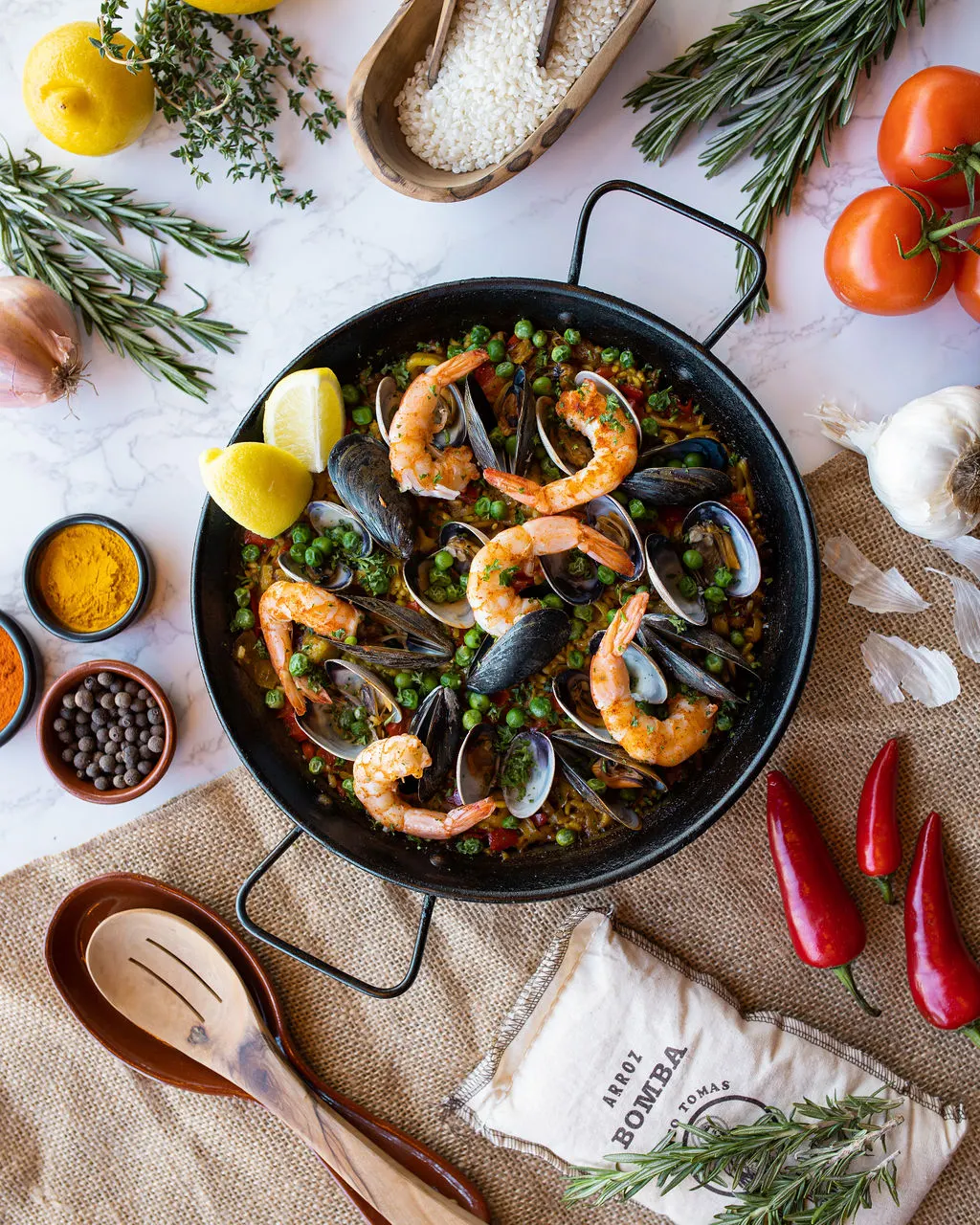 Seafood paella styled with its raw ingredients around the pan - recipe photography by Lemonad Media