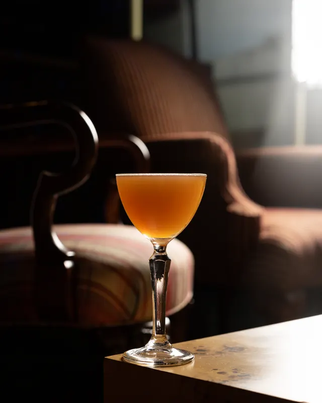 An amber sour in a Nick and Nora glass on the table corner beside a striped armchair at Stereo 41, Walnut Creek