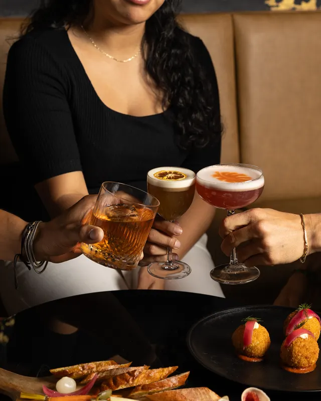 Three cocktails raised together over the plates at Suspiro, Santana Row, San Jose