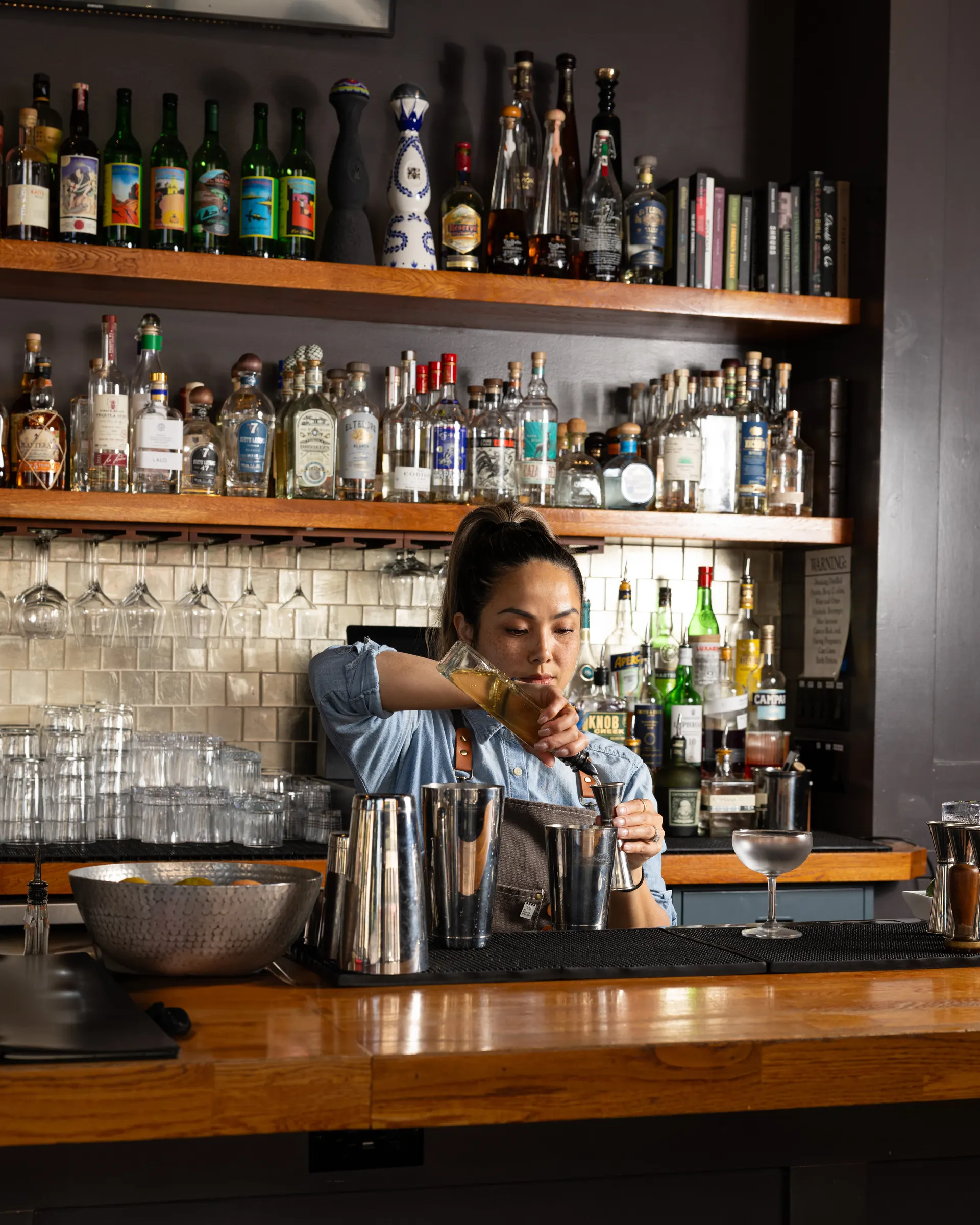 A bartender working the tin in front of the bottle wall at Town Tavern, Alameda