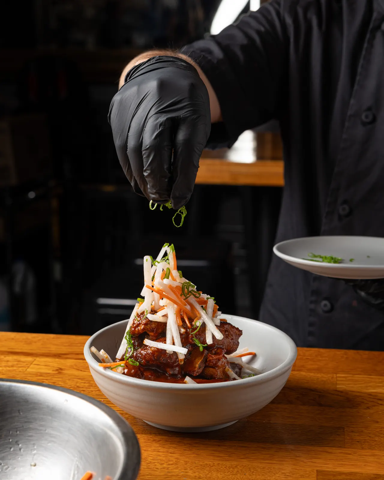 A gloved hand dropping the last garnish on a stacked plate at Town Tavern, Alameda
